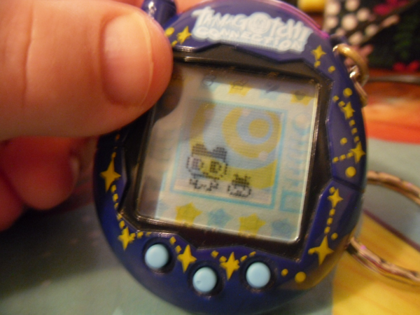 A closeup photo of someone holding a tamagotchi. There are two tamagotchi onscreen, an adult and a baby.